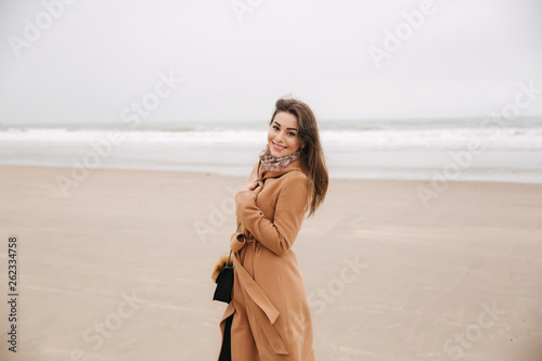 Portrait of beautiful woman walkink along the coast near the north sea. Elegant lady in brown coat with fashion make up stand in front of the sea