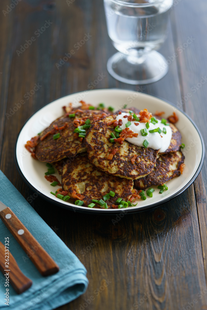 Potato pancakes draniki served with sour cream, chives and bacon on a white plate. Dark wooden table, blue linen napkin, high resolution Potato pancakes draniki served with sour cream, chives and bacon on a white plate. Dark wooden table, blue linen napkin, high resolution
