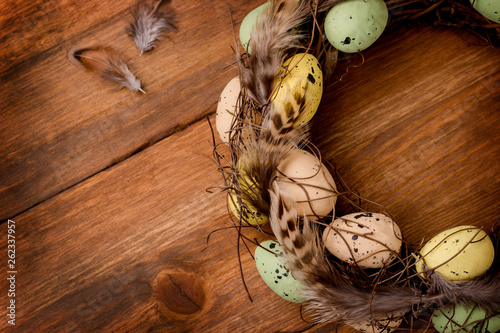 Isolated vine wreath is decorated with bird feathers, quail eggs, on the brown wooden background, Easter scene, composition.