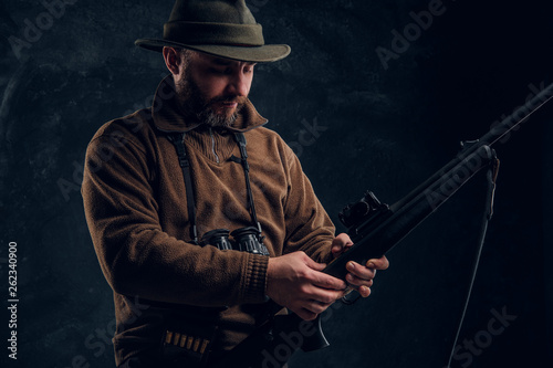 Opening of the spring hunting season. Hunter ready to hunt and charging a hunting rifle. Studio photo against a dark wall background