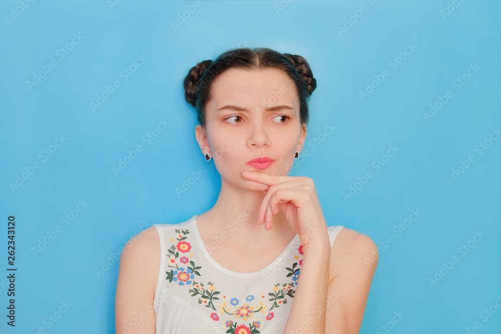 Funny cute girl on a blue studio background. Bright emotional female portrait. Thoughtful face looking away Funny cute girl on a blue studio background. Bright emotional female portrait. Thoughtful face looking away