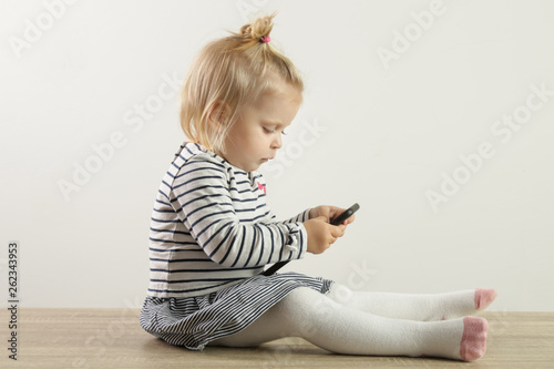 Studio portrait of a cute blonde baby girl holding a cell phone