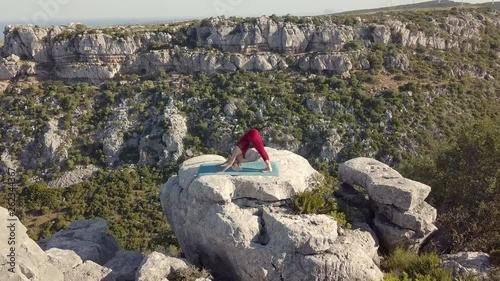 Aerial Footage of Mature Yoga Fitness Woman Performing Downward Facing Dog (Adho Mukha Svanasana) Pose. Standing on a Cliff at Edge of Ravine. Zooming in and Circling Around Model.