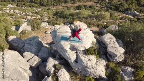 Aerial Footage of Mature Yoga Fitness Woman Performing Downward Facing Dog Pose With Leg Exercises on a Cliff at Edge of Ravine. Free Goats Walking Below. Fixed Viewpoint.