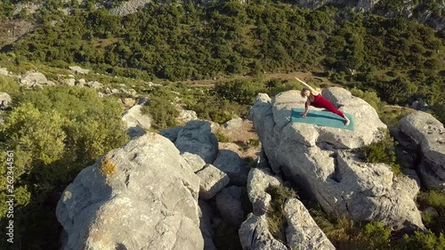 Aerial Footage of Mature Yoga Fitness Woman Performing Warrior Pose (Virabhadrasana), Standing on a Cliff at Edge of Ravine. Camera Circling and Backing Out from Model.