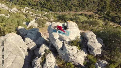 Aerial Footage of Mature Yoga Fitness Woman Performing Downward Facing Dog Pose With Leg Exercises on a Cliff at Edge of Ravine. Free Goats Walking Below. Fixed Viewpoint.