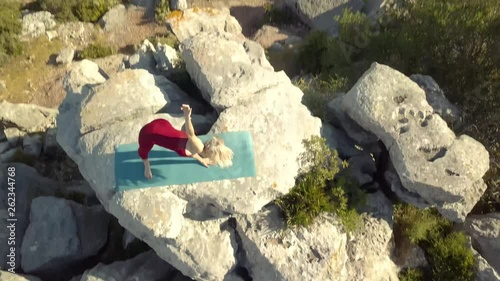 Aerial Footage of Mature Yoga Fitness Woman Performing Triangle Pose (Trikonasana ), Standing on Cliff Edge of Ravine. Camera Moving Above Model Panning Down, Continuing Past Model, Revealing Ravine.