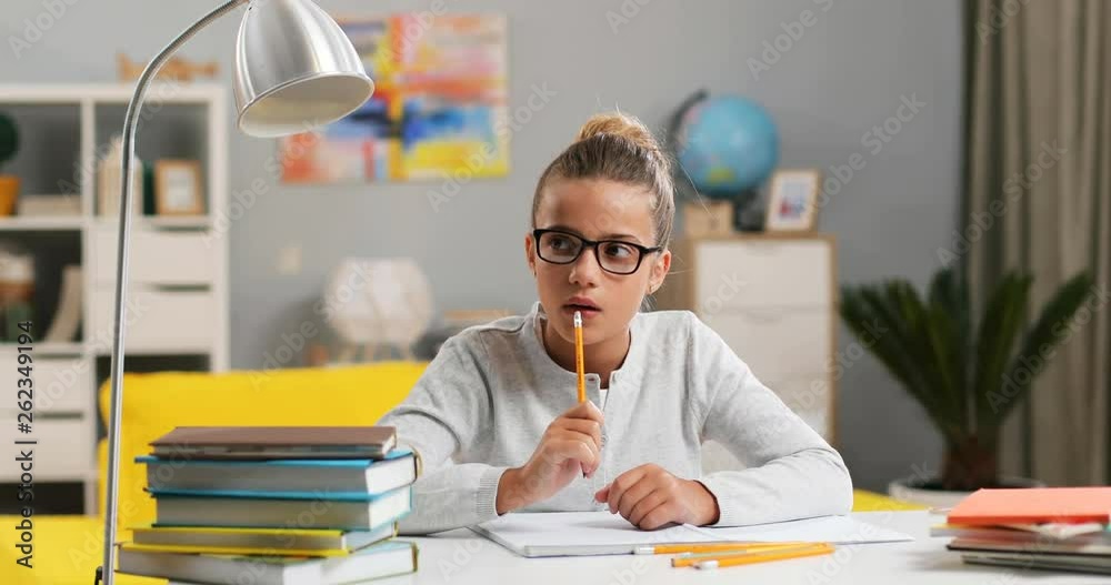 Caucasian pretty small schoolgirl in glasses sitting at the desk in her ...