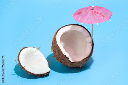 Fresh juicy coconut with a cocktail umbrella isolated on a blue background. Concept of Healthy eating and dieting. Travel and holiday concept