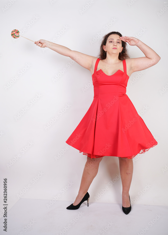 pretty chubby fashion girl wearing red pinup dress and posing with tasty colorful lollipop on white studio background pretty chubby fashion girl wearing red pinup dress and posing with tasty colorful lollipop on white studio background