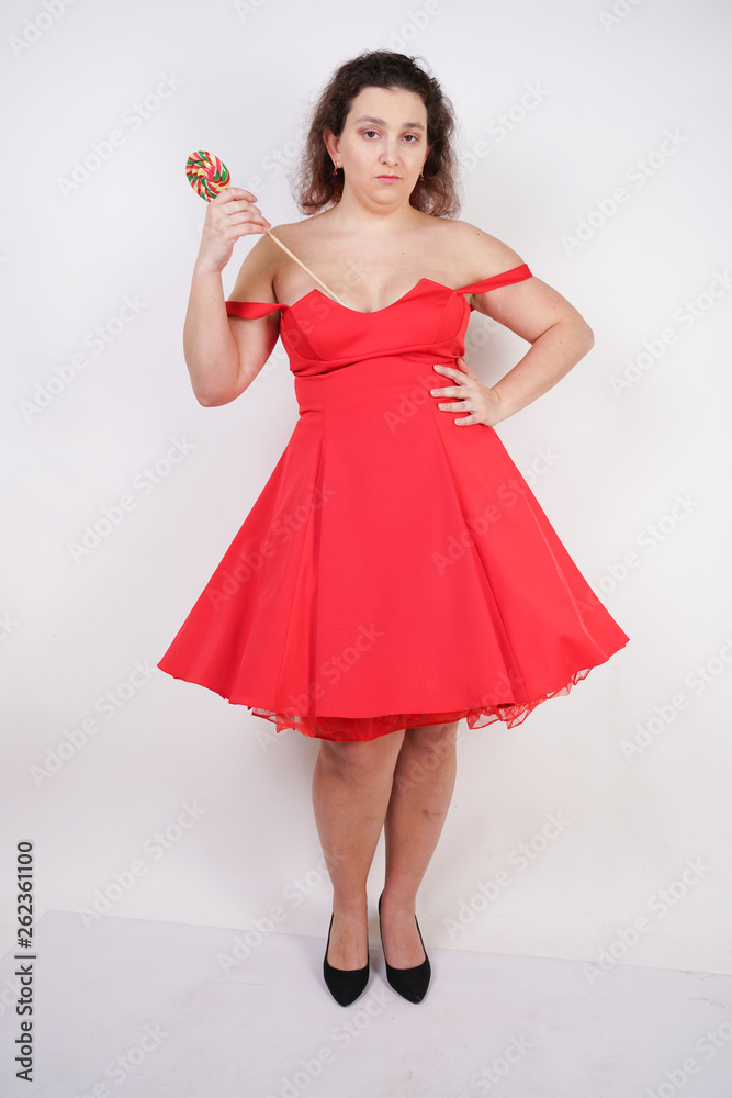 pretty chubby fashion girl wearing red pinup dress and posing with tasty colorful lollipop on white studio background pretty chubby fashion girl wearing red pinup dress and posing with tasty colorful lollipop on white studio background