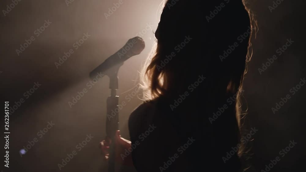 Close-up of the face of the singer with microphone on a black smoky background. The singer sings a song on stage in the dark, smoke, purple light, concert 4k
