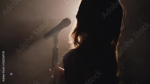 Close-up of the face of the singer with microphone on a black smoky background. The singer sings a song on stage in the dark, smoke, purple light, concert 4k photo