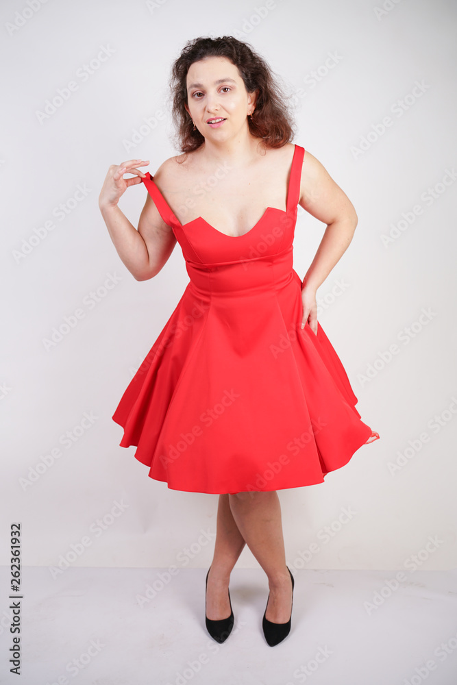 plump woman in a red pinup dress. chubby fashionable girl standing on white background in Studio plump woman in a red pinup dress. chubby fashionable girl standing on white background in Studio