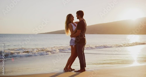 Young attractive couple embracing and kissing on the beach at sunset in slow motion, summer romance