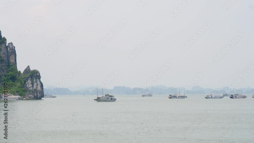 Ship cruising in Halong Bay while other boats are anchored with misty horizon Ship cruising in Halong Bay while other boats are anchored with misty horizon
