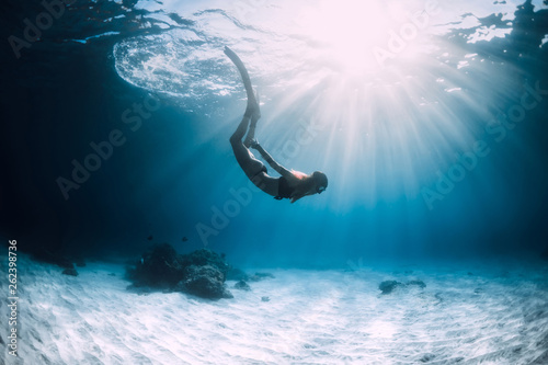 Woman freediver swim with fins over sandy sea.