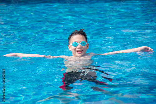 Happy asian boy wearing goggles and swimming at swim pool