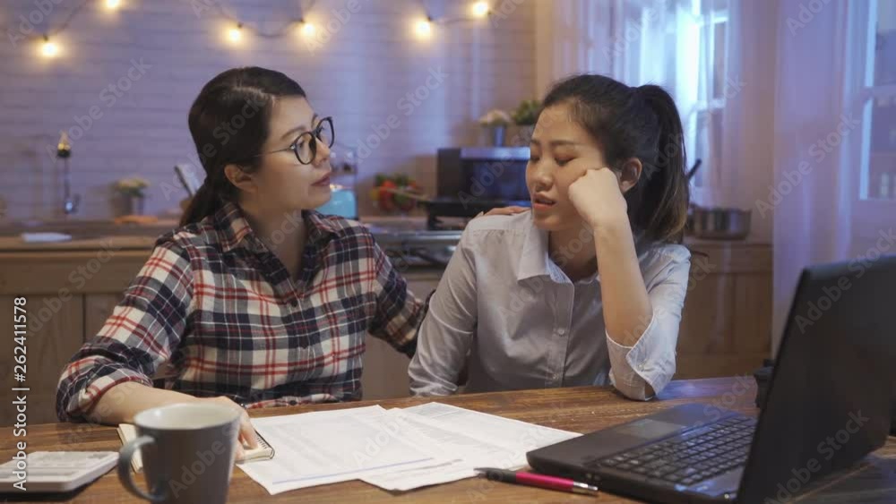 Young woman friend comforting sad depressed businesswoman roommate at kitchen table at home in late night while accounting money by laptop computer and calculator. two girl talking about work trouble Young woman friend comforting sad depressed businesswoman roommate at kitchen table at home in late night while accounting money by laptop computer and calculator. two girl talking about work trouble