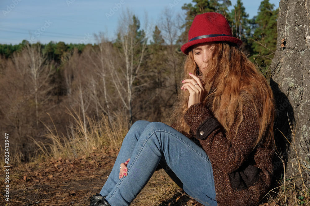 Female model in a red hat and autumn coat in the woods for a walk.