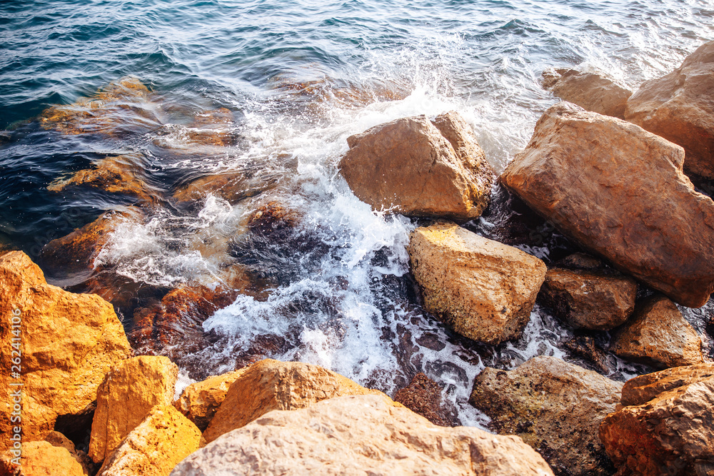 Stormy sea with waves and splashes breaks on sharp stones, warm day, light of sun Stormy sea with waves and splashes breaks on sharp stones, warm day, light of sun
