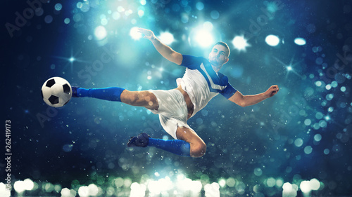 Soccer striker hits the ball with an acrobatic kick in the air on dark blue background