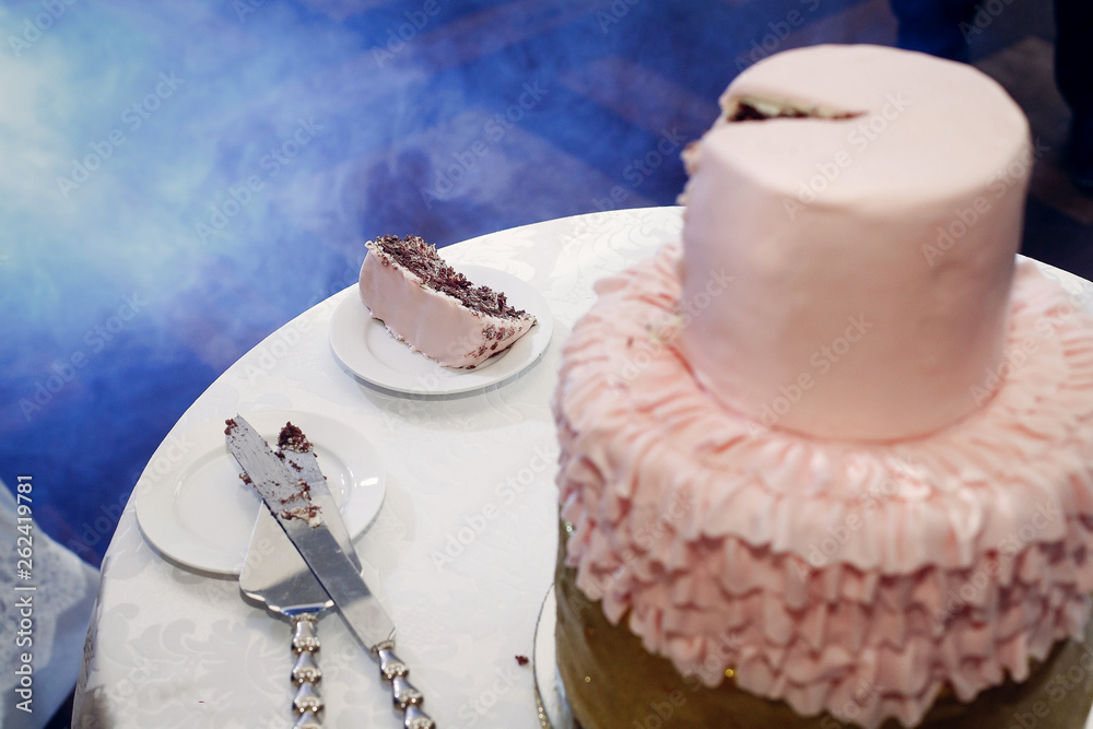 Slice of delicious chocolate wedding cake with gold frosting and pink cream, beautiful decorated wedding cake close-up at restaurant reception