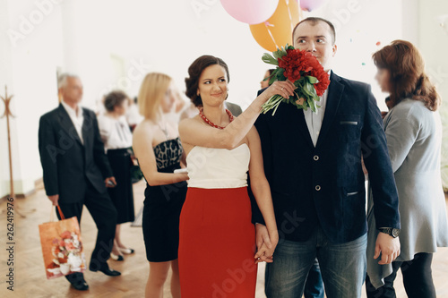 Canvas Print Beautiful funny bride holding hands with handsome groom while pushing bouquet in