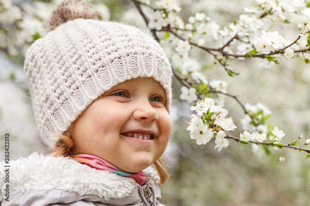 Portrait of a little girl in a white cap near the blooming trees in spring. Portrait of a little girl in a white cap near the blooming trees in spring.