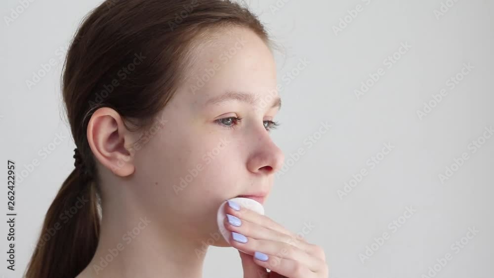 Teenager girl cleans the skin of the face with a cotton swab with