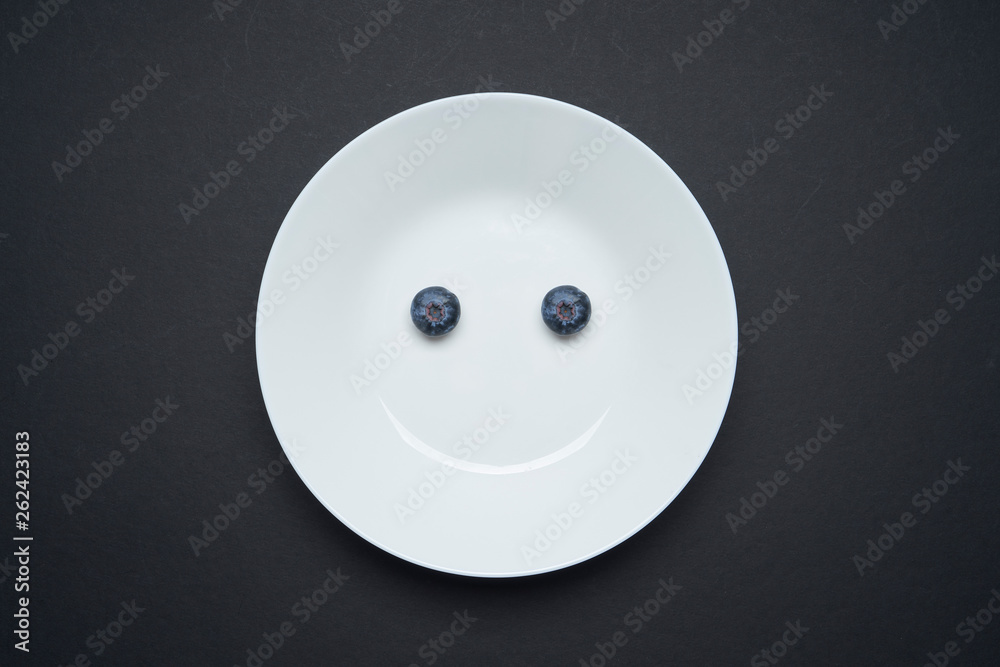 Closeup view of fresh two blueberry on white disc ,black background , smile and happy morning breakfast concept Closeup view of fresh two blueberry on white disc ,black background , smile and happy morning breakfast concept