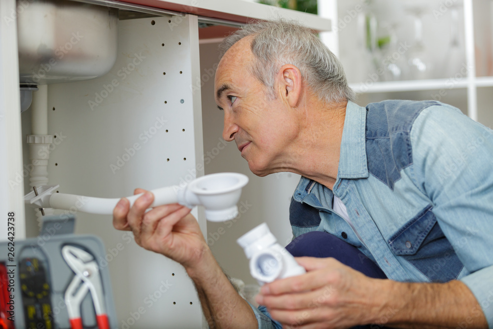 senior citizen using pipe wrench to tighten-up pipes under sink senior citizen using pipe wrench to tighten-up pipes under sink