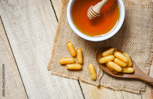 Royal jelly capsules in wooden spoon on sack background and honey in cup
