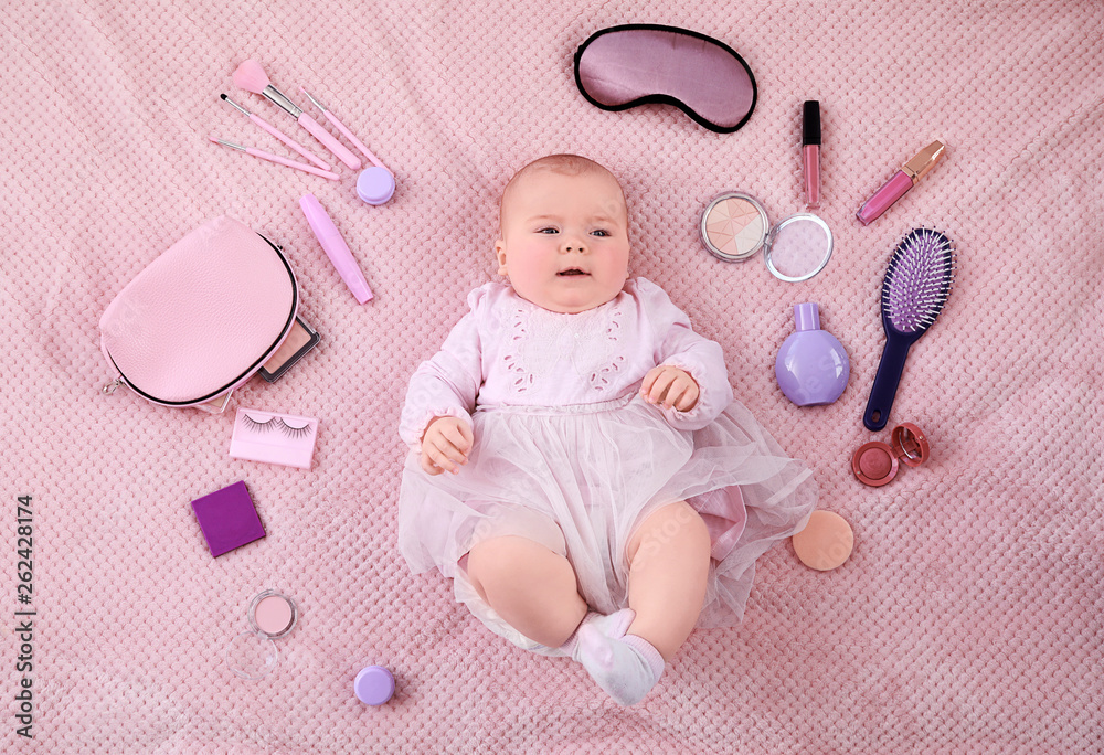 Adorable baby girl with makeup cosmetics and accessories lying on soft