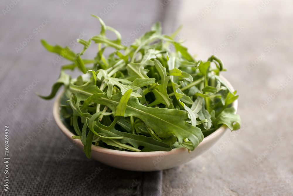 Bowl with tasty fresh arugula on grey table Bowl with tasty fresh arugula on grey table