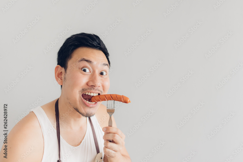 Happy man is eating the delicious favorite sausage he cooked himself. Happy man is eating the delicious favorite sausage he cooked himself.