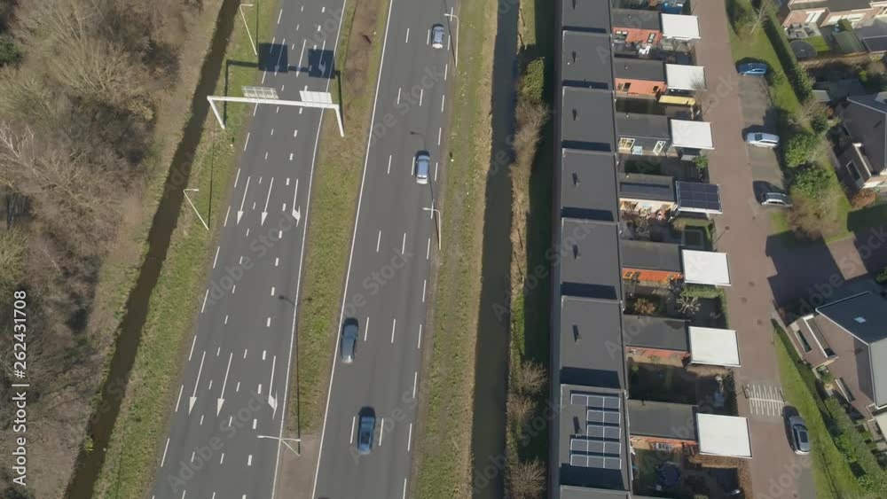 Aerial drone view of traffic passing by a 7 lane road with houses as sound barrier