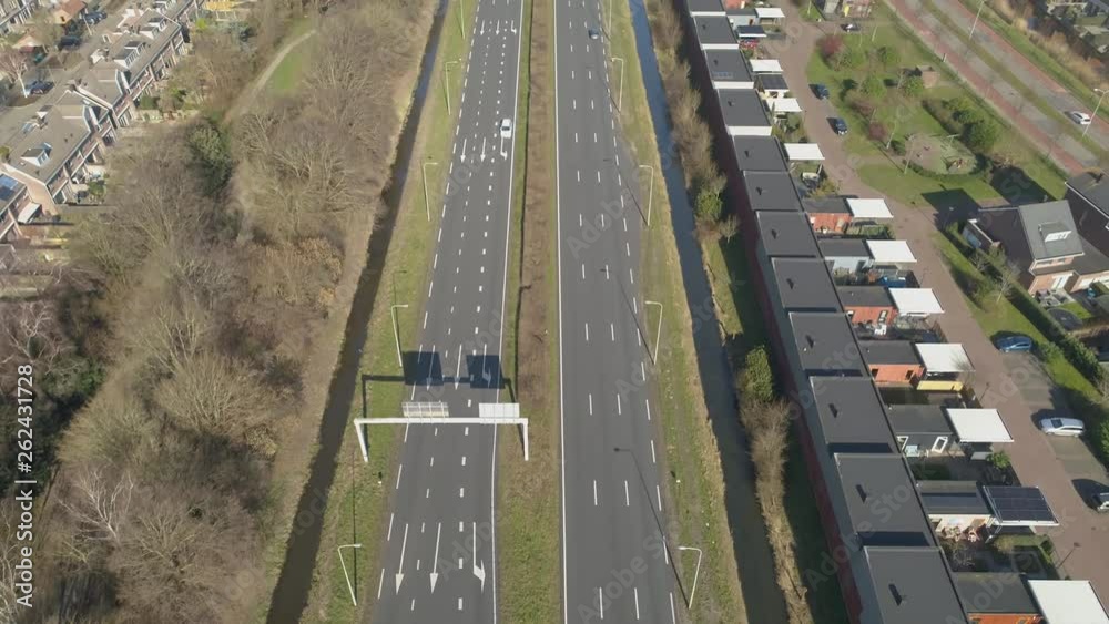 Aerial drone view of traffic passing by a 7 lane road with houses as sound barrier