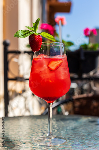 A refreshing red drink with ice  strawberry and mint in a wine glass on a city cafe terrace