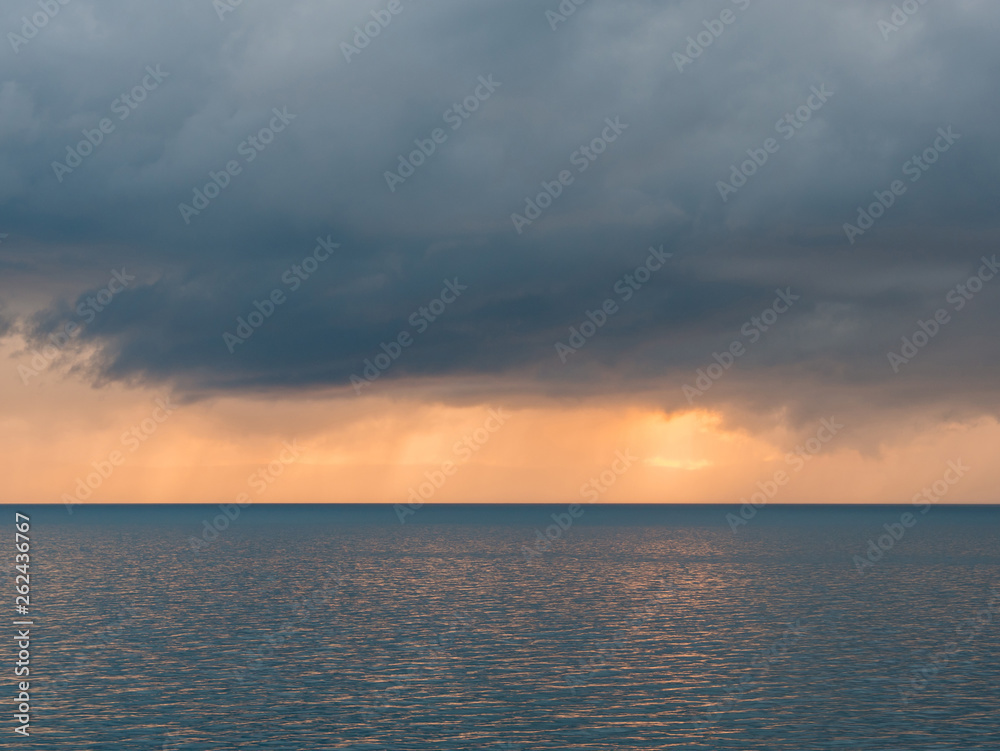 Dark clouds over calm sea at sunset