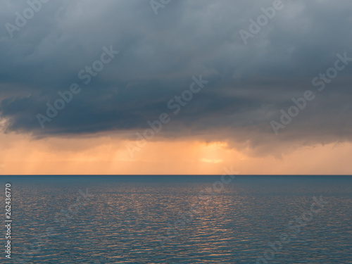 Dark clouds with sunlight over calm sea at sunset