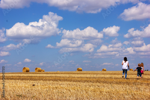 Summer sunny day. Mom and kids are walking along the harvested wheat field.