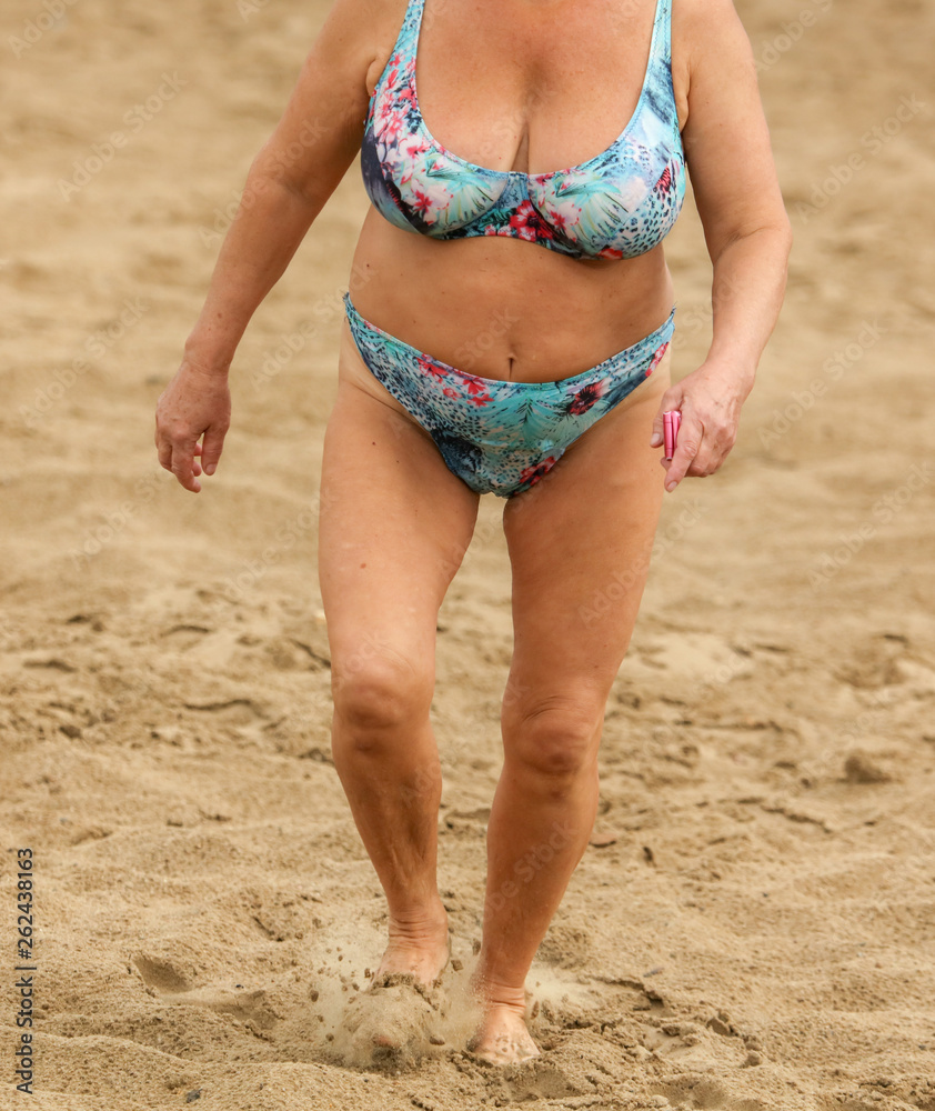 Old woman in swimsuit walking along the beach Stock Photo | Adobe Stock