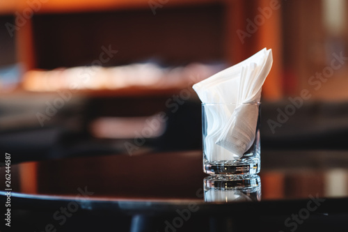 Glass with crumpled white tissues on brown coffee table. Blurred background and bokeh lights. Selective focus on the glass. 