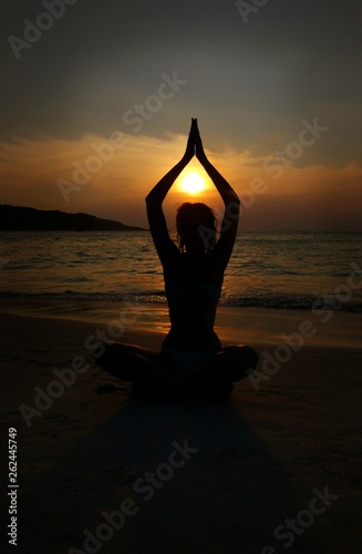 Silhouette of a girl who sits in a yoga pose at sunset on the beach with his hands above his head