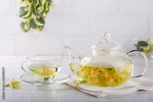 Linden tea in a transparent tea pot. Glass tea pot with herbal lime tree tea on white background. Medicinal plant, flowers used for herbal teas and tinctures.