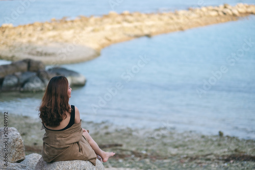 A beautiful asian woman enjoy sitting on the rock by the seashore
