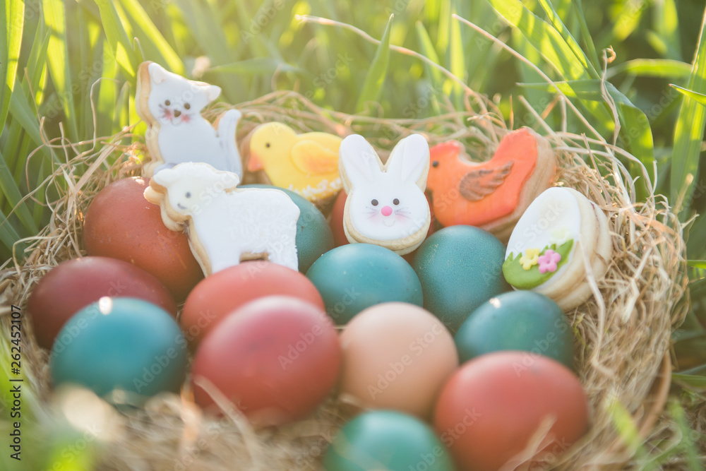 cute easter decoration and colorful painted easter eggs in a basket placed in a green grass with backlight spring concept