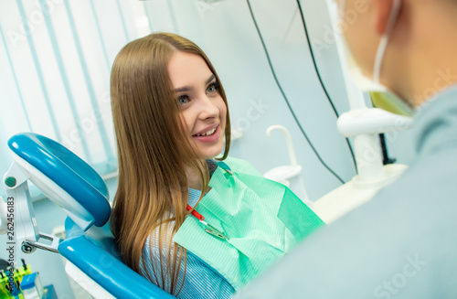 A beautiful girl is sitting in the dental chair and looking at a man doctor who is talking to her. dental clinic