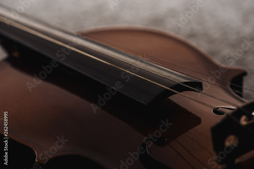 close up of strings on wooden violoncello in darkness on grey textured background